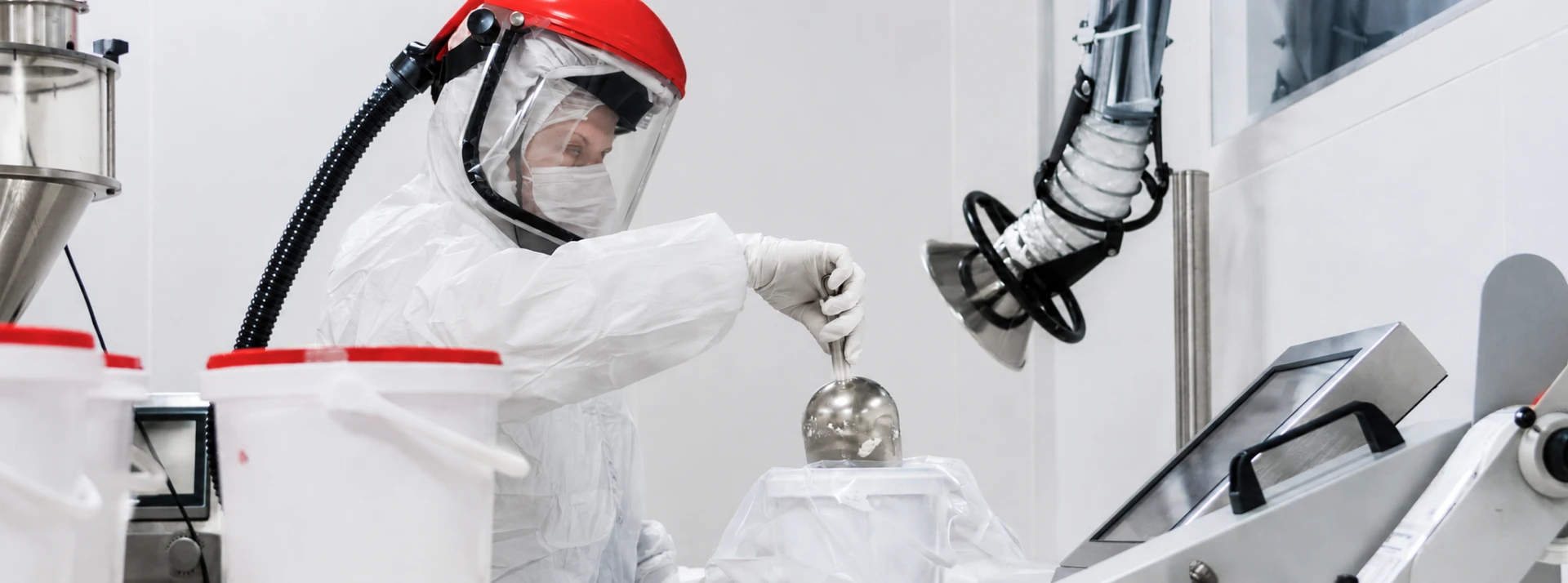 Compounding technician in protective gear working in a bright pharmaceutical clean room
